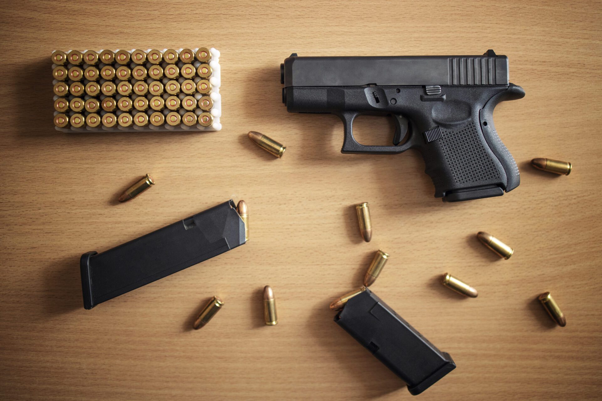 Gun with box of ammunition and bullets on wooden background.